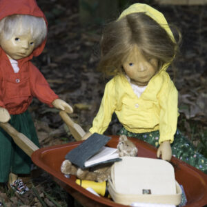 two hand carved wooden dolls pushing a wheelbarrow full of their belongings