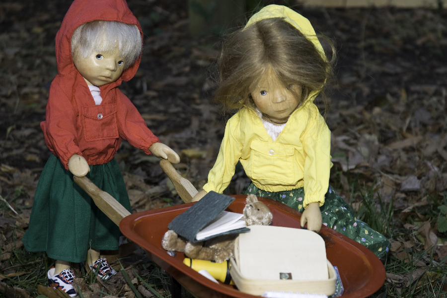 two hand carved wooden dolls pushing a wheelbarrow full of their belongings