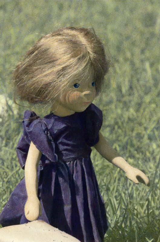 a hand carved wooden doll, in a purple dress